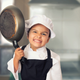 Little girl in chef's uniform holding up skillet